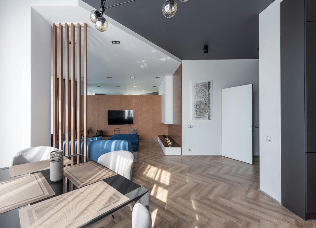 Interior of spacious flat with chairs at table placed near living room with couch and TV at wall with decorations