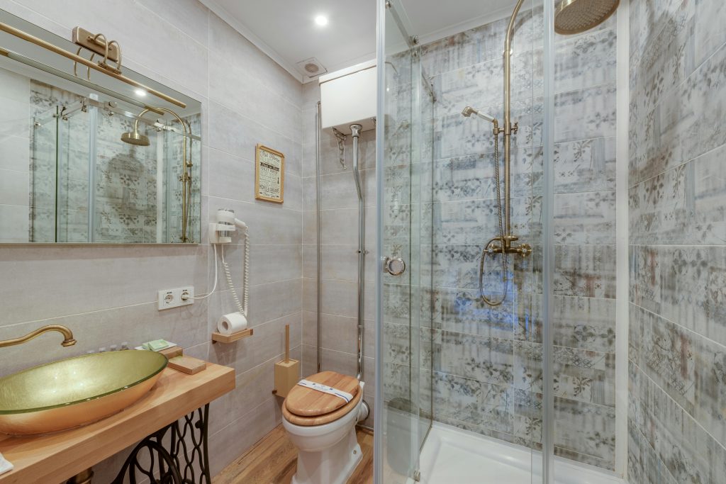 Modern bathroom with glass shower, wooden elements, and brass accents for a luxurious feel.