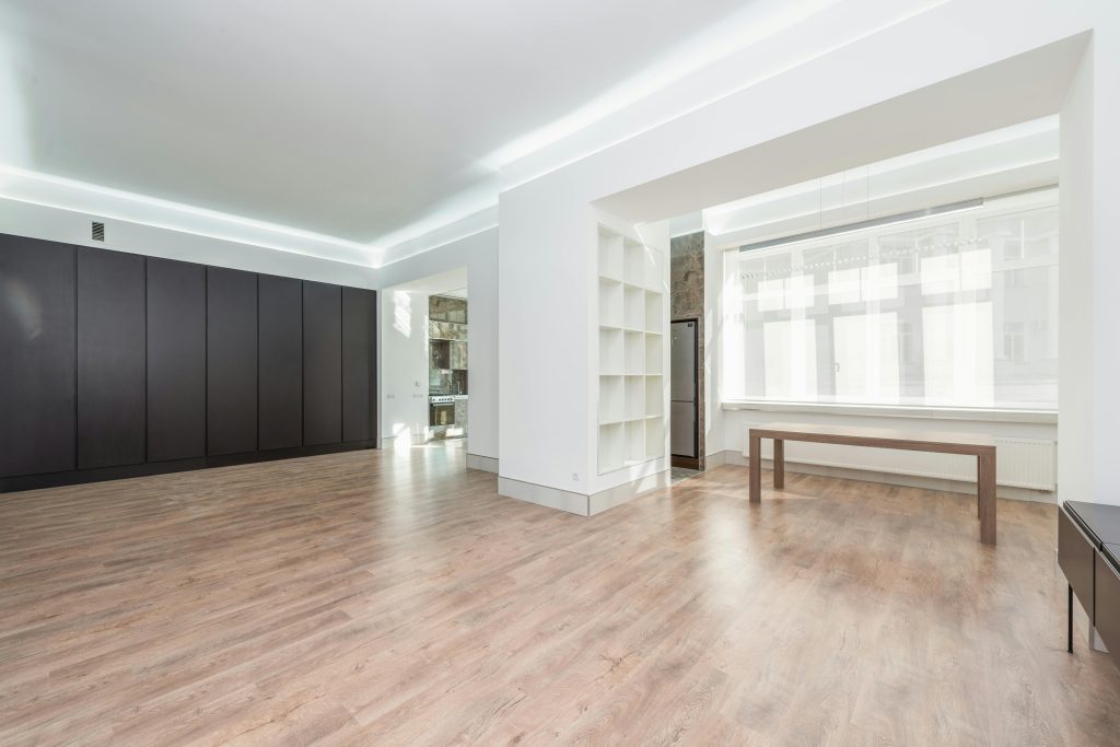A modern minimalist room interior with hardwood flooring and sunlight streaming in through large windows.